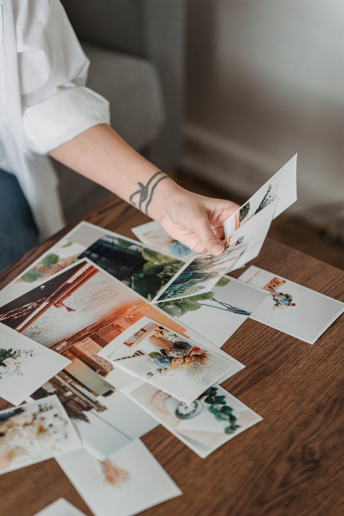 ours-journey High angle anonymous female looking through printed pictures scattered on table in light room